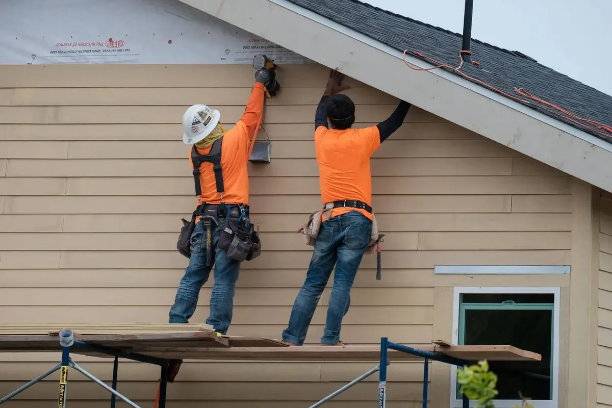 Two siding installers on scaffolding replacing lap siding with Tyvek housewrap visible behind